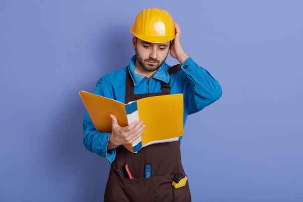 Construction engineer hold yellow paper folder read information about new project, do not understand details, looks at documents with puzzled facial expression. - Photo, Image