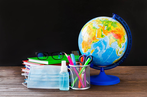 Back to school during quarantine. School supplies with medical mask and sanitizer on chalkboard background. Education concept. Copy space - Fotó, kép