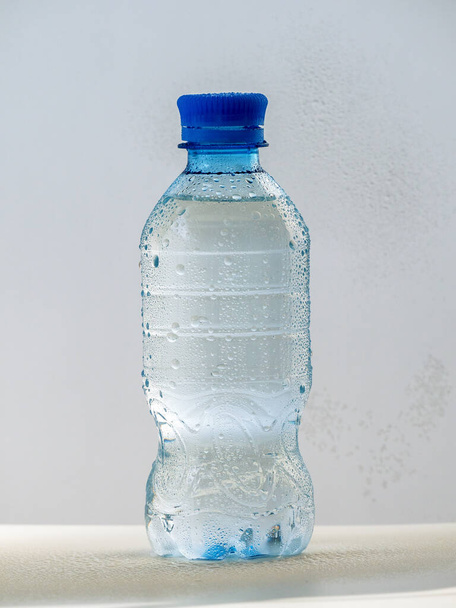 Пластикова пляшка з чистою холодною водою на світлому фоні. Пляшка закрита кришкою. На пляшці видно краплі води
. - Фото, зображення