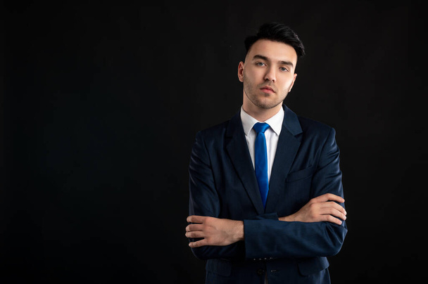 Portrait of business man wearing blue business suit and tie standing with arms crossed isolated on black background with copy space advertising area - Fotoğraf, Görsel