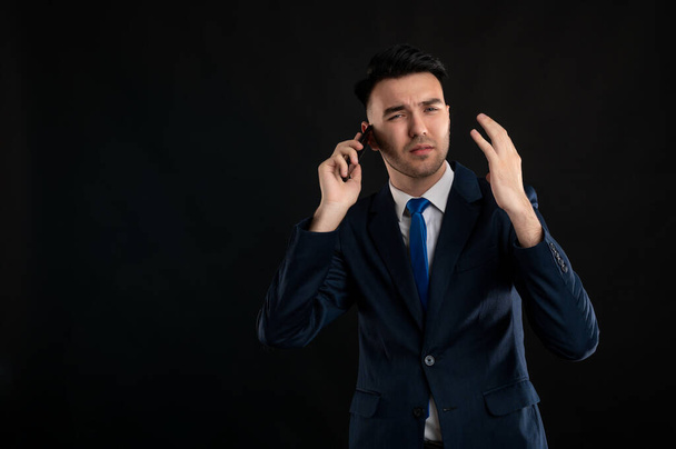 Portrait of angry business man wearing blue business suit and tie talking on the phone isolated on black background with copy space advertising area - Foto, Bild