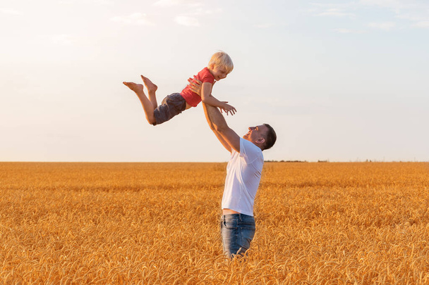 Junger Vater spielt mit seinem Sohn im Weizenfeld. Glückliche Vaterschaft und unbeschwerte Kindheit. Feld aus reifem Weizen - Foto, Bild