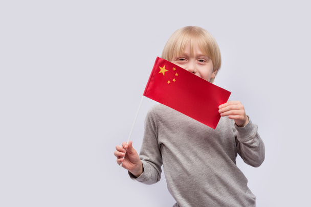 Gyermek portré fehér háttérrel, kínai zászlóval a kezében. Kínai nyelv tanulása gyerekeknek. - Fotó, kép