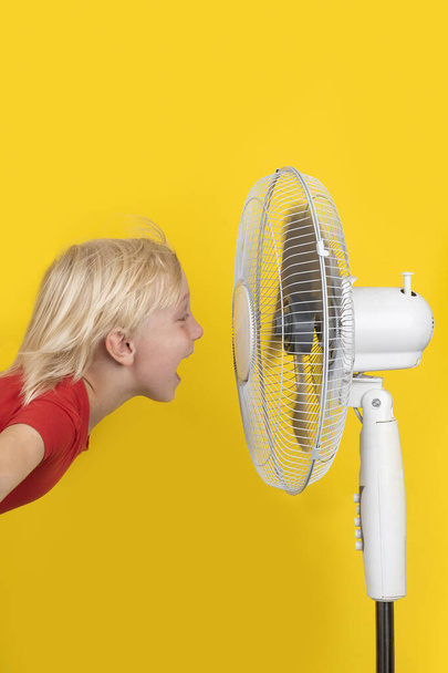 Enfant avec ventilateur sur fond jaune. Cadre vertical. Été chaud. - Photo, image