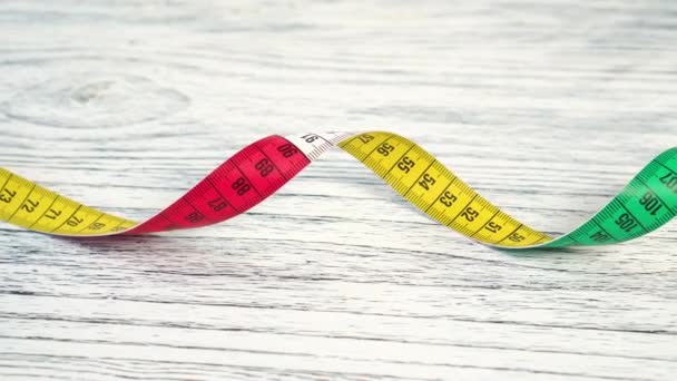 Close-up of a twisted bright multicolored measuring tape, centimeter on a wooden background. Close-up. Diet health concept - Footage, Video