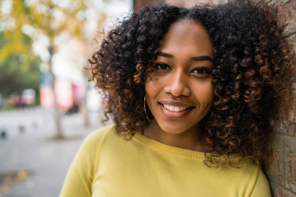 Πορτρέτο της όμορφης νεαρής αφρο-αμερικανικής γυναίκας με σγουρά μαλλιά στέκεται σε εξωτερικούς χώρους στο δρόμο. - Φωτογραφία, εικόνα