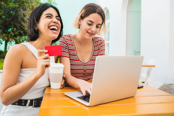 Portrait of two young friends doing online shopping with laptop and credit card at coffee shop. Shop online concept. - Photo, image