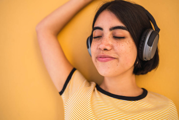 Portrait of young latin woman listening to music with headphones against yellow background. Urban concept. - Foto, Imagen