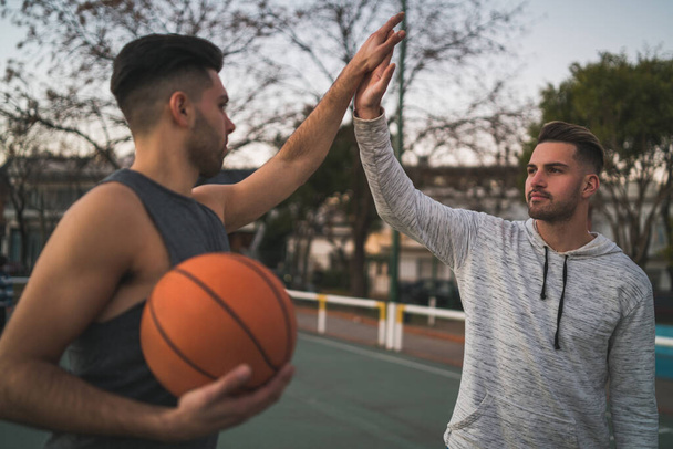 Portrait of two young friends playing basketball and having fun on court outdoors. Sport concept. - 写真・画像