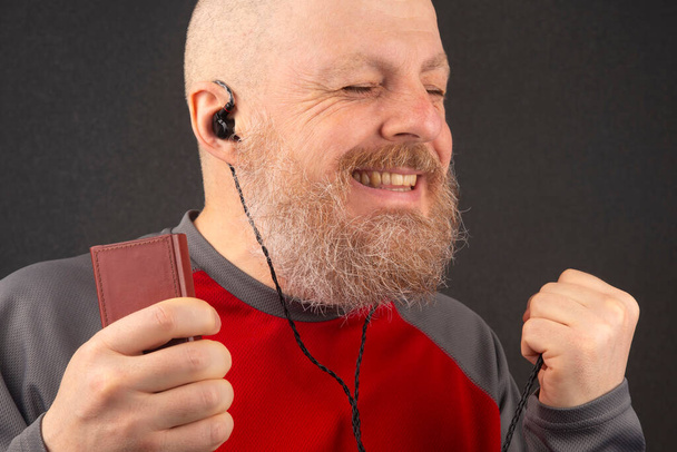 Der bärtige Mann hört seine Lieblingsmusik am liebsten zu Hause mit einem Audio-Player in kleinen Kopfhörern. Musikliebhaber und Musikliebhaber. Musik und Hi-Fi-Sound. - Foto, Bild