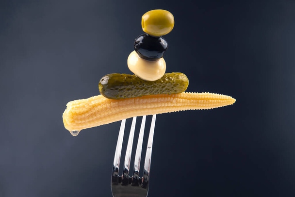 Oliwki, ogórek marynowany, grzyby i kukurydza na widelcu zbliżenie na ciemnym tle. żywność i warzywa - Zdjęcie, obraz