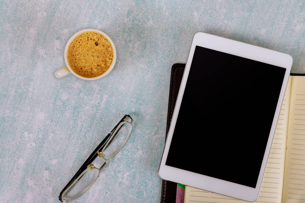 Trabajar en el escritorio de la oficina con una tableta digital con taza de porcelana de café negro, anteojos, cuaderno semanal - Foto, Imagen