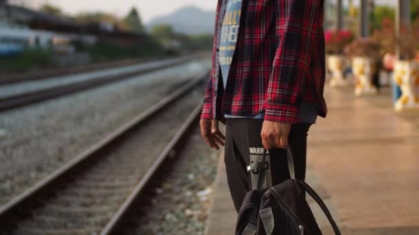 Kesäpäivä Aasian mies istuu ja puhuu älypuhelin ja odottaa junan mennä matkustaa auringonnousun - Materiaali, video