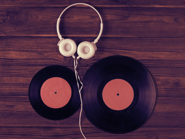 Twee vinylschijven en een witte koptelefoon met een draad op een houten ondergrond. - Foto, afbeelding