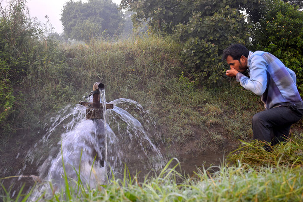 Agricultural equipment for field irrigation, an Indian farmer drinking water from water jet overflowing on his farm, Rain fog, selective focus - Fotoğraf, Görsel
