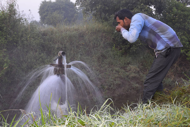 matériel agricole pour l'irrigation des champs, un agriculteur indien qui boit l'eau du jet d'eau débordant sur sa ferme, brouillard pluvial, foyer sélectif - Photo, image