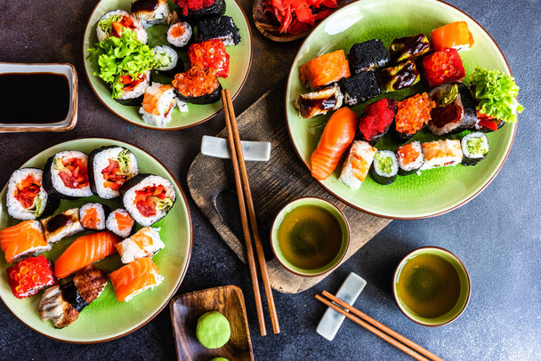 комплект суши с различными сашими, суши-роллы и чай подается на каменной доске - Фото, изображение