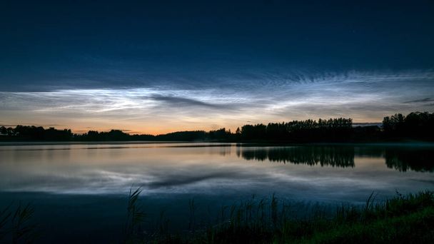 湖の上に白い銀の雲と美しい夜の風景,ぼやけた前景,湖の水の中に魅力的な雲の反射,夏の夜 - 写真・画像