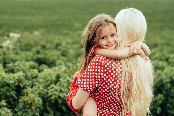 Junge Mutter mit ihrer kleinen Tochter im roten Polka-Dot-Kleid, Spaß auf dem Feld außerhalb der Stadt, Mutterschaft und Kindheitskonzept - Foto, Bild