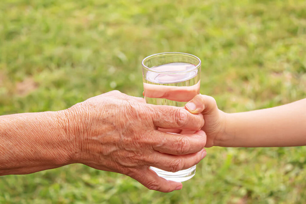 Бабушка дала ребенку стакан чистой воды. Селективный фокус. - Фото, изображение