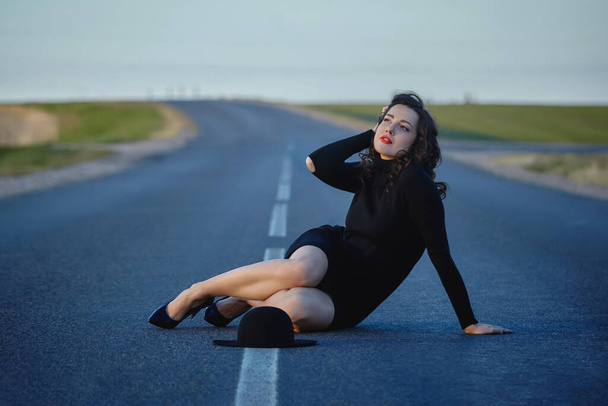 attractive girl in black dress and hat posing on the road with a dividing strip - Photo, Image