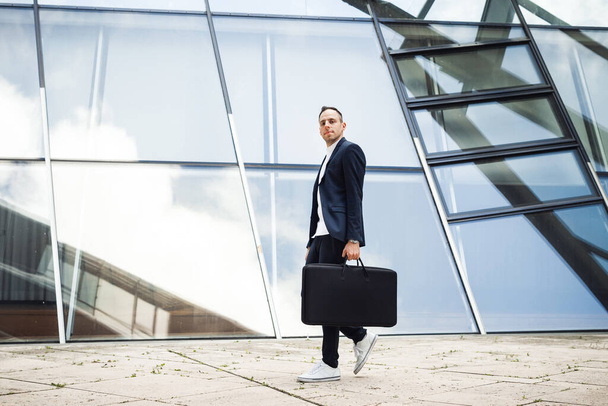 Επιχειρηματίας με μπλε κοστούμι και μαύρη τσάντα. Άνθρωπος ματιά στην κάμερα σε μεγάλο φόντο παράθυρο - Φωτογραφία, εικόνα
