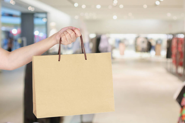 Frau hält Einkaufstasche mit verschwommenem modischen Boutique-Bekleidungsgeschäft Schaufenster in Einkaufszentrum - Foto, Bild
