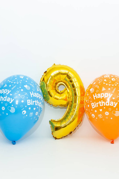 Número inflável 9 cor dourada metálica brilhante com balões azuis e amarelos isolados no fundo branco. Close-up. Tiro vertical
. - Foto, Imagem