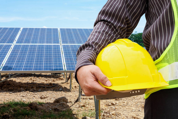 Young business man engineer hold yellow helmet at solar panel power plant construction site background - Photo, Image