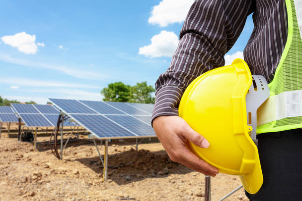 Jonge zakenman ingenieur houden gele helm op zonnepaneel elektriciteitscentrale bouwplaats achtergrond - Foto, afbeelding