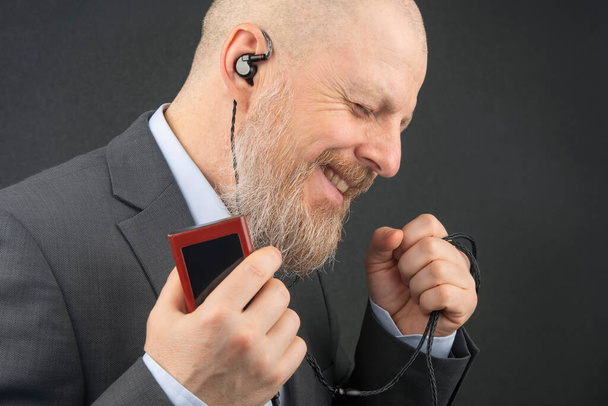 γενειοφόρος επιχειρηματίας θέλει να ακούει την αγαπημένη του μουσική στο σπίτι με ένα ακουστικό player σε μικρά ακουστικά. ακουστόφιλος και λάτρης της μουσικής. μουσική και hi-fi ήχος - Φωτογραφία, εικόνα