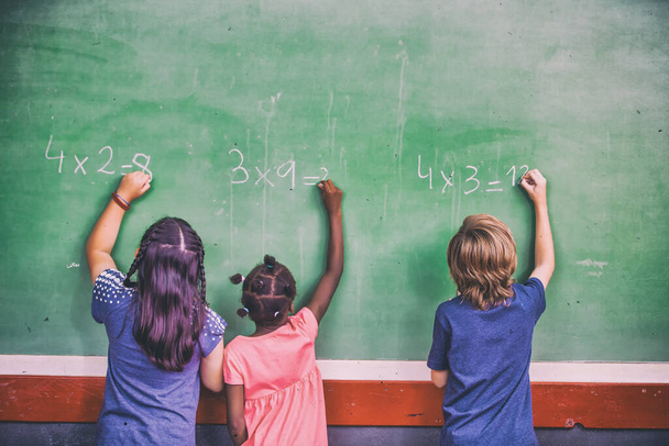 Tři žáci mnohonárodnostní školy v učebně na tabuli, zadní pohled. Návrat do školy. - Fotografie, Obrázek