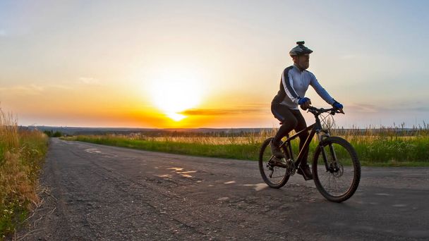 ciclista paseos en el camino hacia la puesta del sol. deportes y aficiones. actividades al aire libre - Foto, Imagen