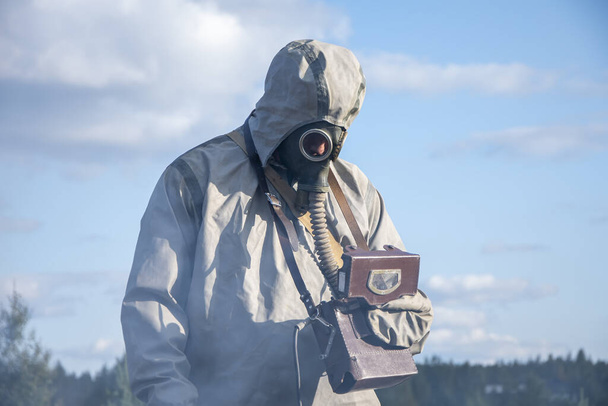 Ένας στρατιωτικός με στολή χημικής προστασίας μετρά την ακτινοβολία με ένα δοσίμετρο. - Φωτογραφία, εικόνα
