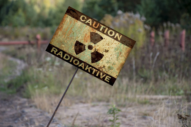 Egy jel ragadt a földbe a szavakkal: óvatosság, sugárzás, szögben. Figyelmeztető jel radioaktív veszélynek kitett területen. - Fotó, kép