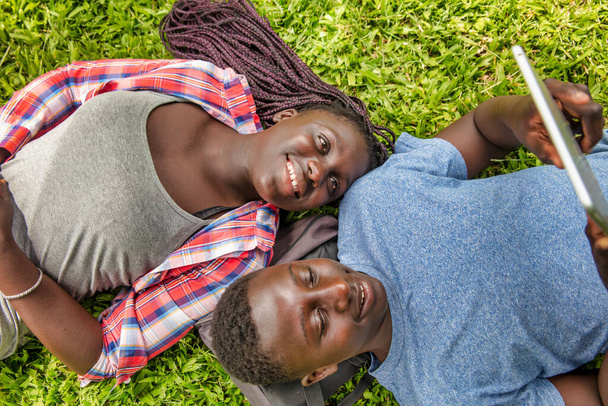 Two african teenagers lying on the grass using tablet. Bak to school concept - Photo, Image