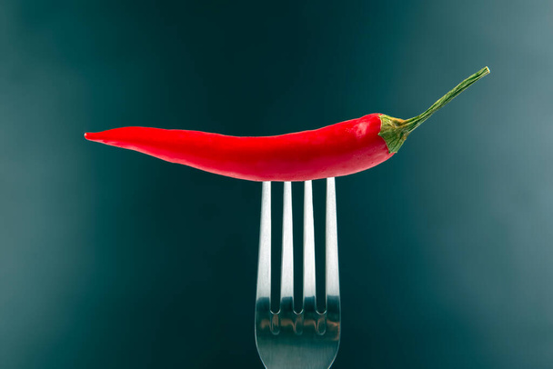 Red hot pepper with fork close-up on dark background. Healthy vegetable food and vitamins - Fotografie, Obrázek