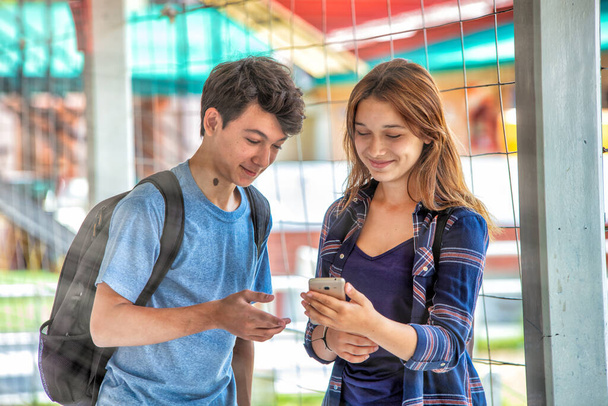 Zwei befreundete kaukasische Teenager kehren glücklich in die Schule zurück. Mädchen, die etwas am Telefon zeigen. Zurück zum Schulkonzept. - Foto, Bild