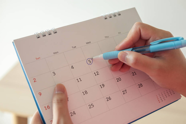 Mão com caneta marca no dia 5 na data do calendário com círculo azul
 - Foto, Imagem