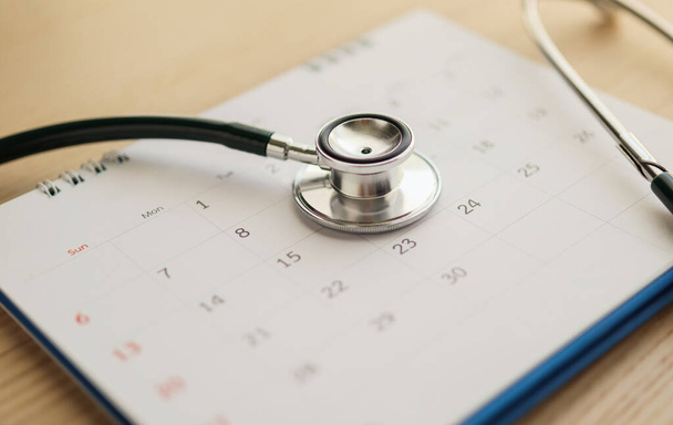 Stethoscoop met kalenderpagina datum op houten tafel achtergrond arts afspraak medisch concept - Foto, afbeelding