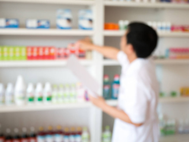 wazig beeld van apotheker die geneesmiddelen van de plank haalt in de apotheek - Foto, afbeelding