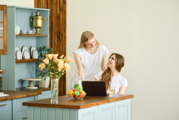 Two beautiful students making video conference call sitting in the kitchen - Foto, Bild