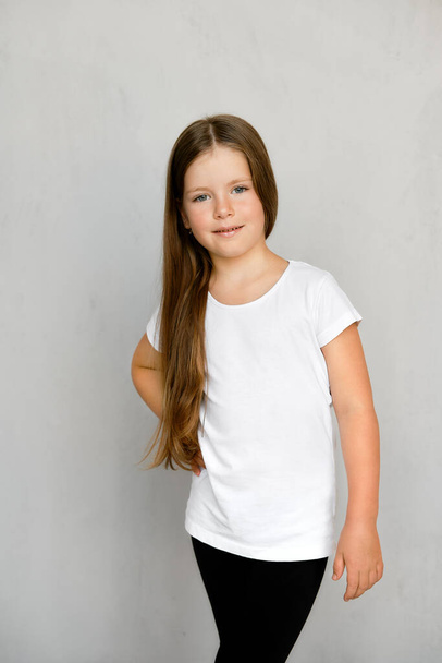 Lindo niño pequeño con pelo largo en camiseta blanca y pantalones de chándal negros posando  - Foto, Imagen