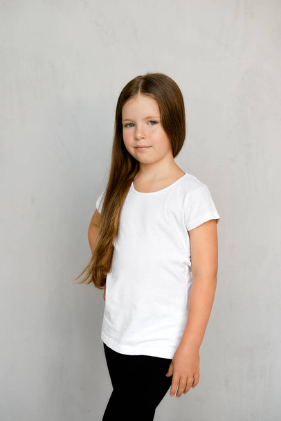 Cute young child with long hair in white t-shirt and black sweatpants posing  - Valokuva, kuva
