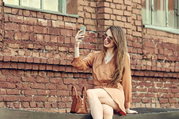 Happy young woman sitting on bench and making selfie with mobile phone - Fotoğraf, Görsel
