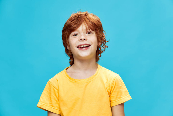 Glückliches Kind mit roten Haaren lacht auf isoliertem blauen Hintergrund  - Foto, Bild