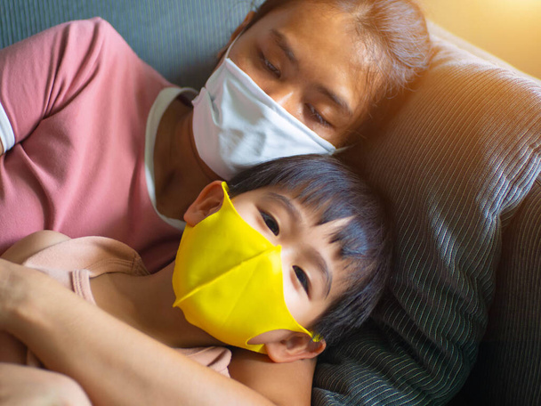 Covid-19, γυναίκα και ο γιος της μολυνθεί με coronavirus ασθένεια του ύπνου, Γυναίκα και ο γιος της φορώντας μάσκα προσώπου κοιμάται στον καναπέ, φορώντας μάσκα προσώπου για την προστασία από coronavirus, έκθεση επιχειρήσεων. Εργασία από το σπίτι. - Φωτογραφία, εικόνα