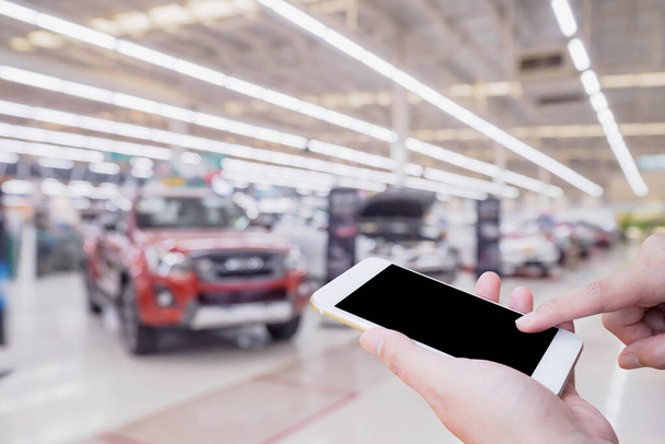 hand houden mobiele smartphone met wazige rij van nieuwe auto 's in de showroom dealerovereenkomst abstracte gedeconcentreerde achtergrond - Foto, afbeelding