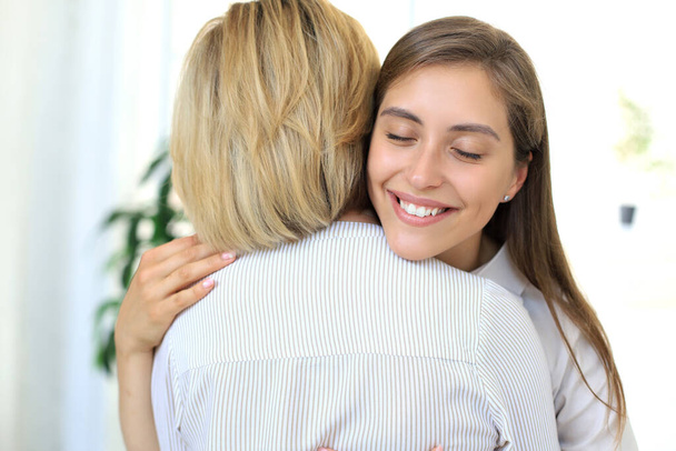 Cheerful young woman is embracing her middle aged mother in living room - Foto, imagen