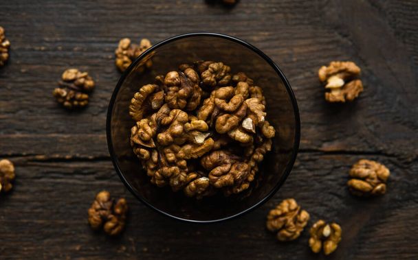 Walnut in a smale plate with scattered shelled nuts and whole nut which standing on a wooden vintage table. Walnuts is a healthy vegetarian protein nutritious food. Walnut on rustic old wood. - Foto, Bild